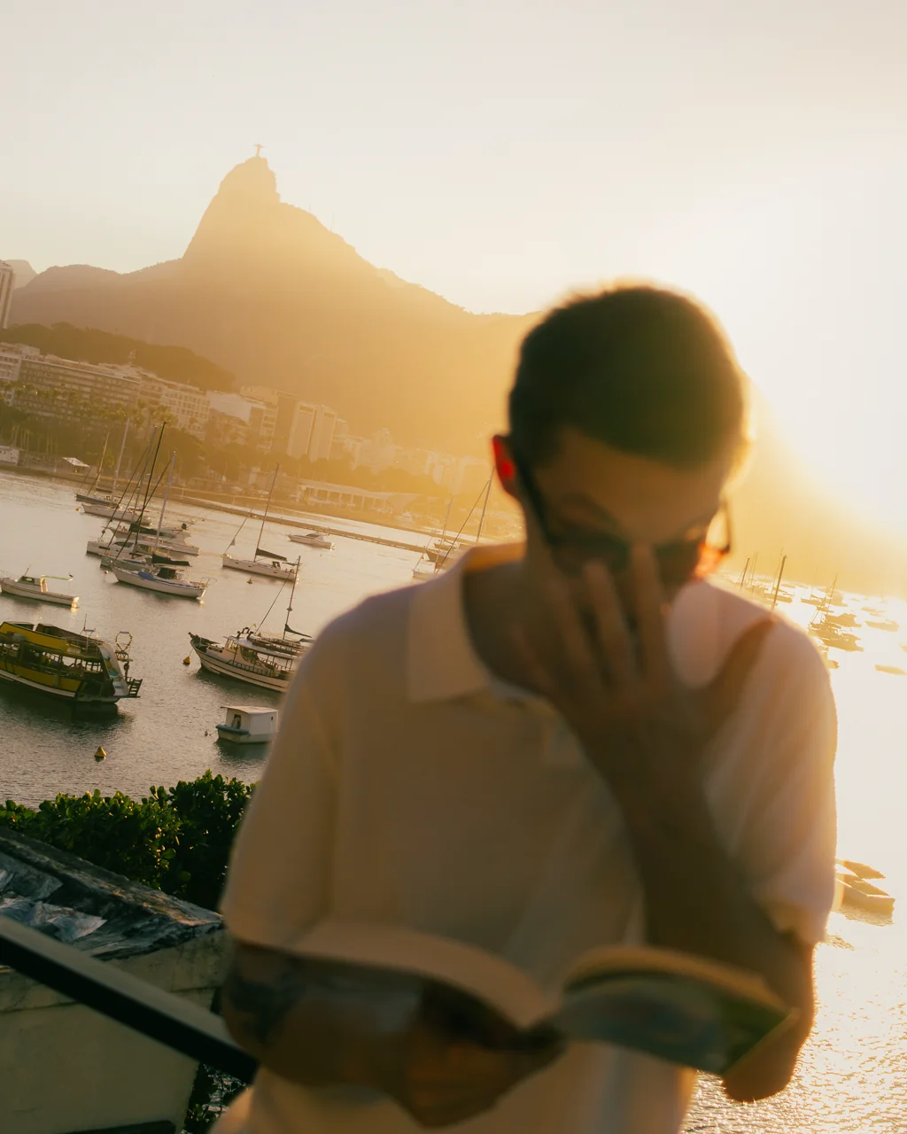 Homem lendo ao pôr do sol no terraço com o Cristo Redentor ao fundo, Hotelinho da Urca