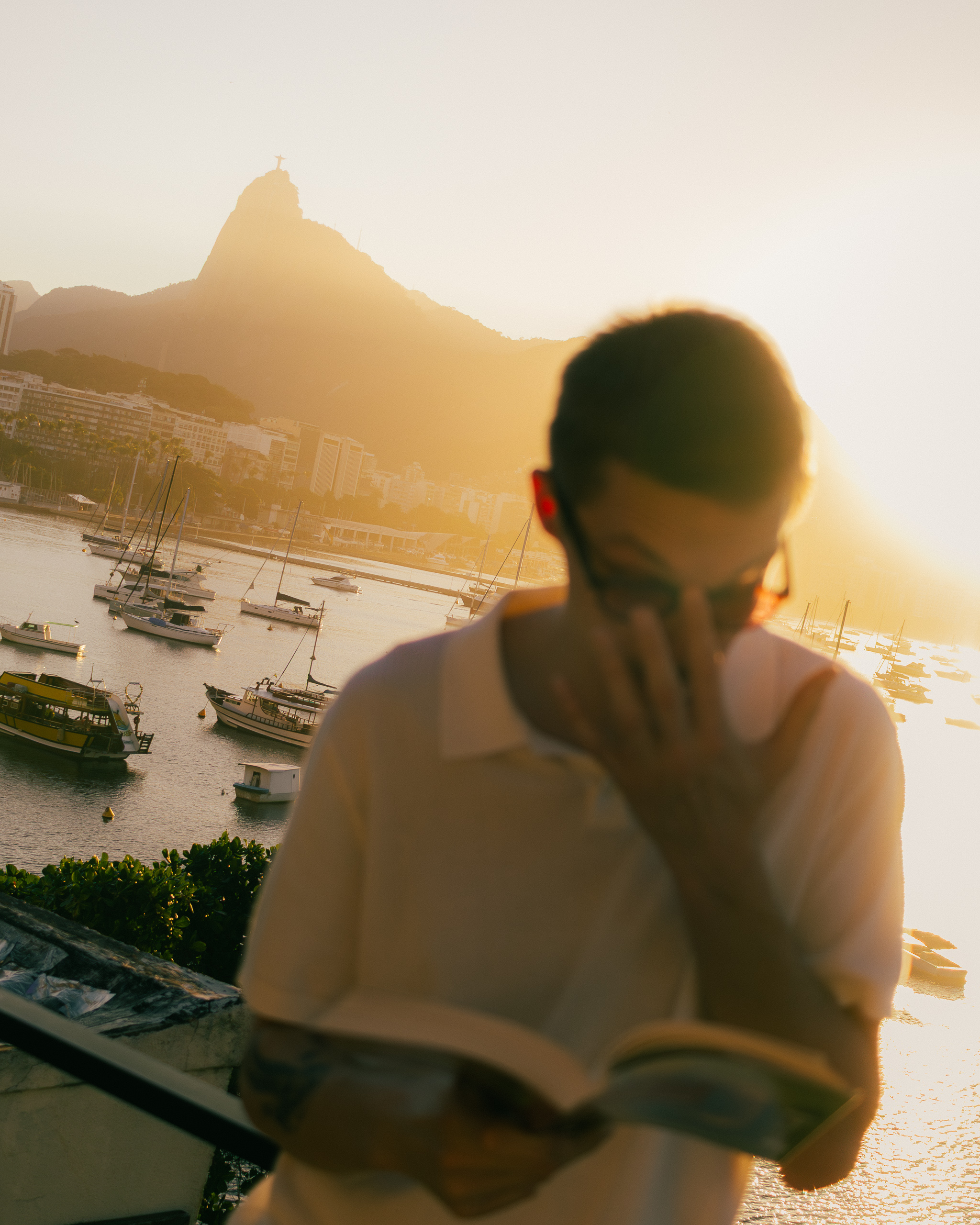 Homem lendo ao pôr do sol no terraço com o Cristo Redentor ao fundo, Hotelinho da Urca