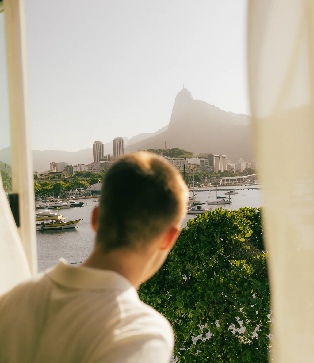 Hóspede de costas na janela com vista para o Cristo Redentor e a baía de Botafogo, Hotelinho da Urca
