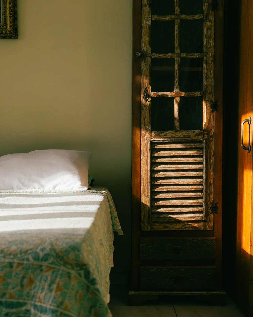 Cama com colcha estampada e armário rústico de madeira em luz dourada, Hotelinho da Urca